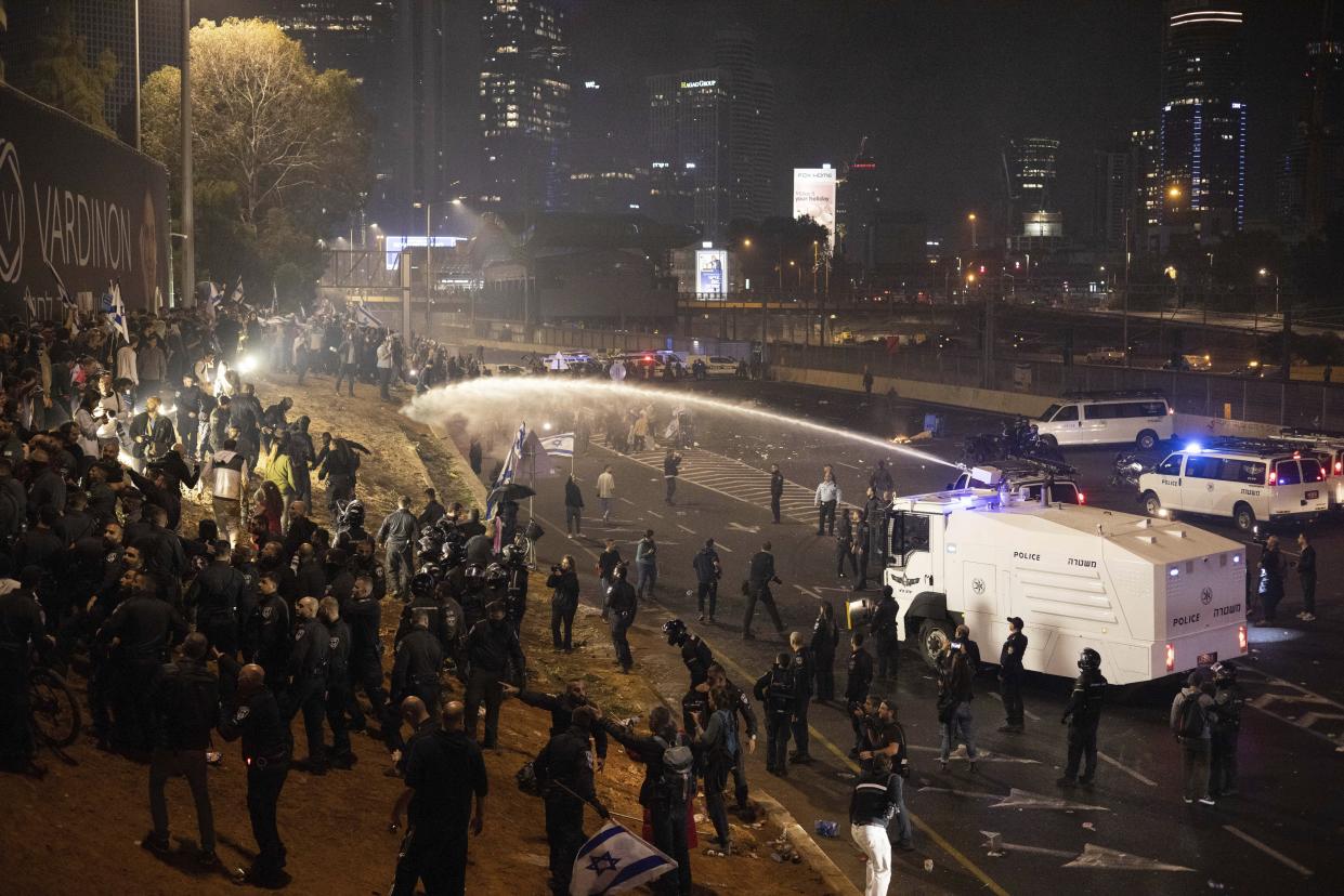 Israeli police use a water cannon to disperse demonstrators blocking a highway during a protest against plans by Prime Minister Benjamin Netanyahu's government to overhaul the judicial system in Tel Aviv, Israel, Monday, March 27, 2023. Tens of thousands of Israelis have poured into the streets across the country in a spontaneous outburst of anger after Prime Minister Benjamin Netanyahu abruptly fired his defense minister for challenging the Israeli leader's judicial overhaul plan. (AP Photo/Oren Ziv)