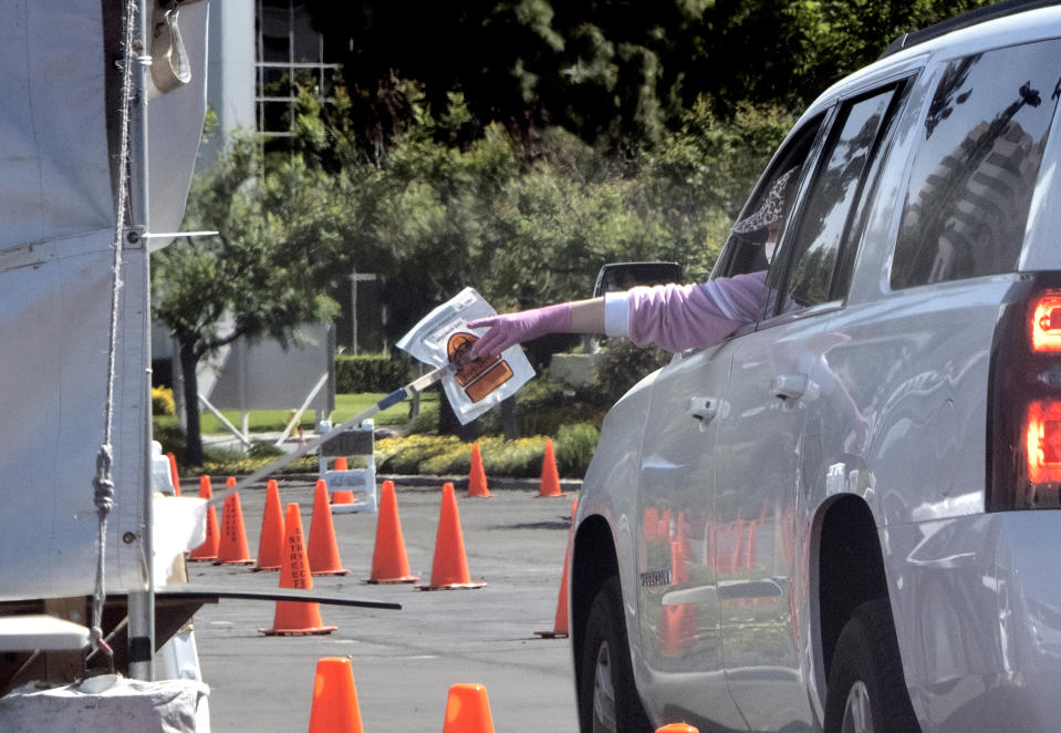 In this Wednesday, May 6, 2020 photo a medical worker passes a self administered coronavirus test on a pole to a passenger in a car at a drive through testing site in the Woodland Hills section of Los Angeles. The city of Los Angeles is providing free coronavirus tests to anyone who wants one regardless of whether they have symptoms. The offer reflects a parting with state guidelines after the mayor partnered with a startup testing company. The test the city is offering is easier to administer and doesn't require the scarce supplies that have created bottlenecks for expanded testing across California. (AP Photo/Richard Vogel)