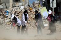 Palestinian volunteers sweep the rubble of buildings, recently destroyed by Israeli strikes, in Gaza City's Rimal district on May 25