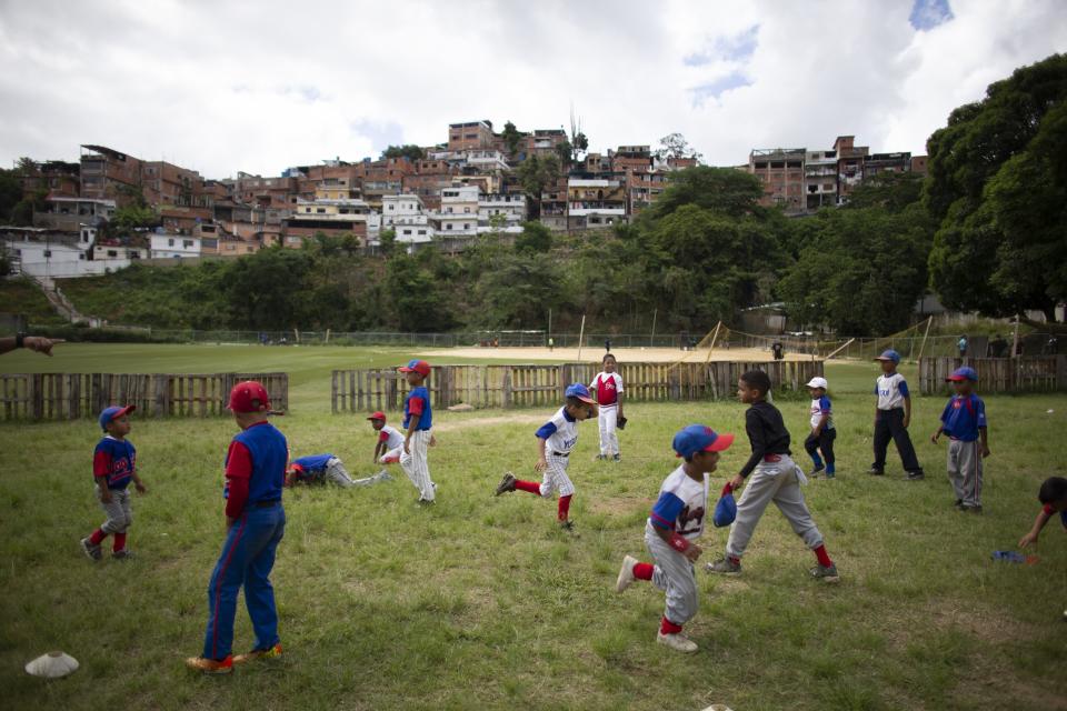In this Aug. 12, 2019 photo, young baseball players run laps during a practice at Las Brisas de Petare Sports Center, in Caracas, Venezuela. Boys run hard, lift weights, bat and pitch in the heat on the baseball field at next to the biggest slum in Caracas. (AP Photo/Ariana Cubillos)