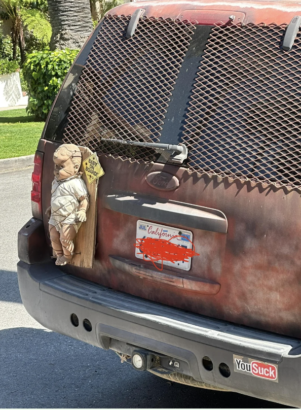 A truck's rear window features a decal simulating a child and dog peering out. Bumper stickers and a license plate are visible