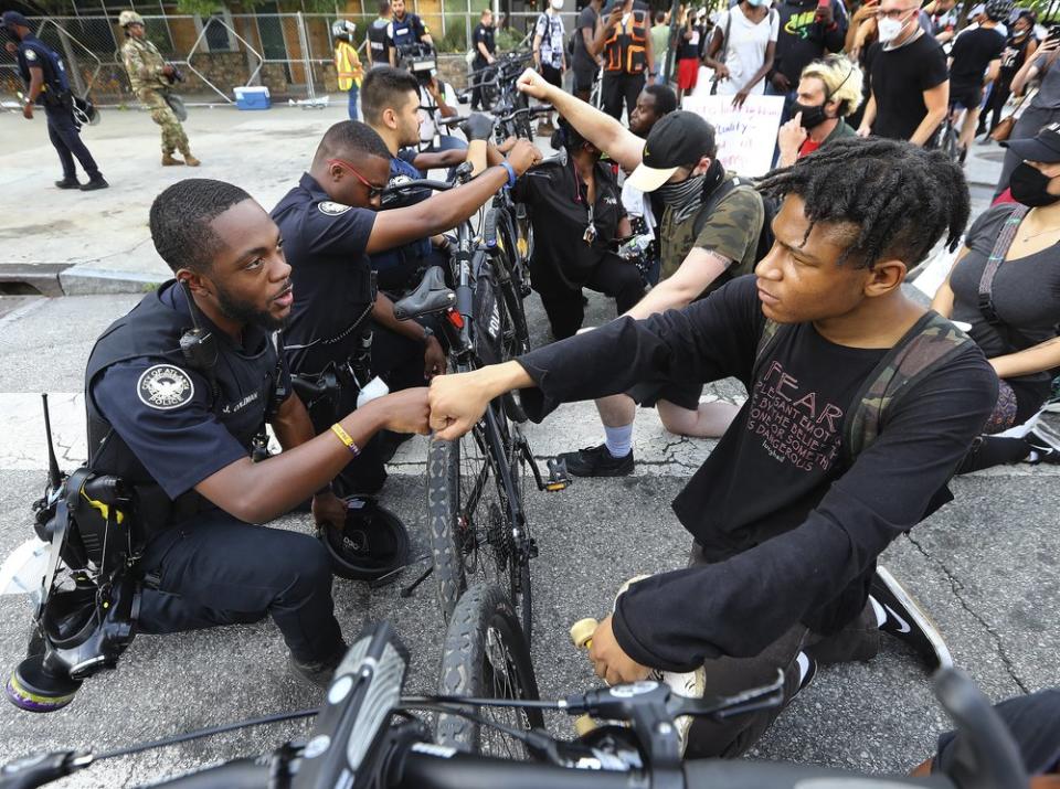 Atlanta police officer J. Coleman, left, and protester Elijah Raffington fist bump while officers kneel down with protesters in a symbolic gesture of solidarity outside the CNN Center, Wednesday, June 3, 2020, in Atlanta during a protest sparked by the May 25 death of George Floyd in Minneapolis police custody. (Curtis Compton/Atlanta Journal-Constitution via AP, File)