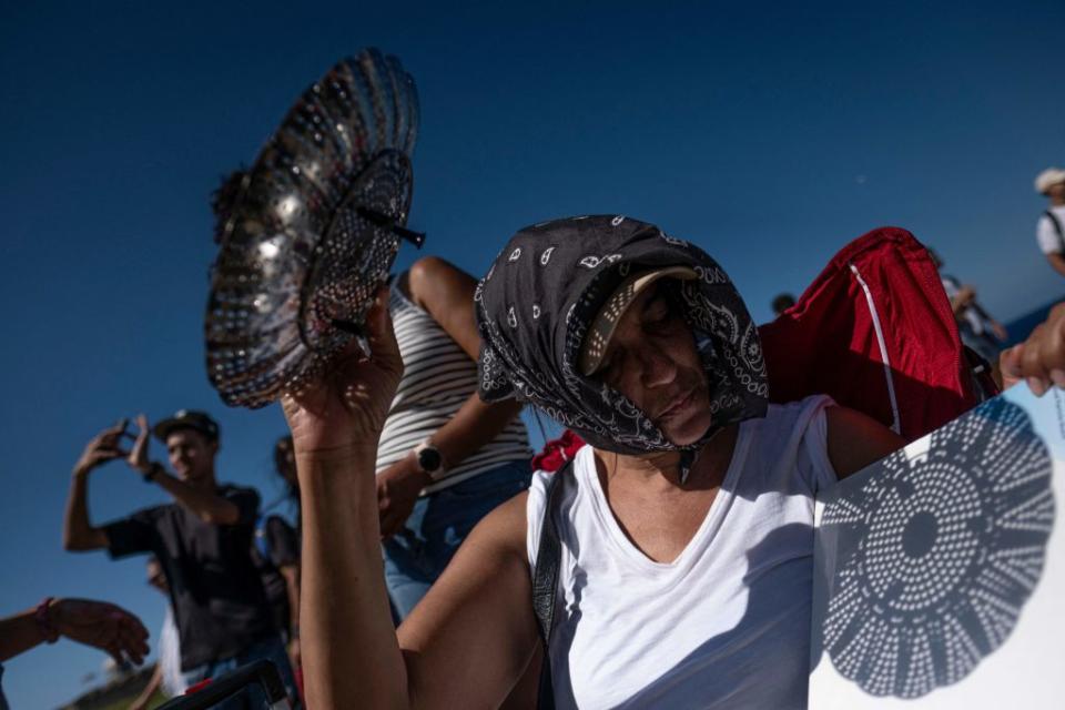 A woman uses a kitchen colander to cast the shadow of the sun on a white board during the annular solar eclipse