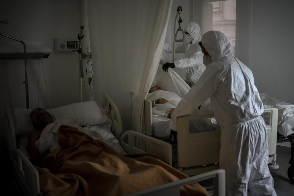 Wearing protective suits to prevent infection, funeral home workers remove the body of an elderly person who died of COVID-19 at a nursing home while another resident sleeps in his bed in Barcelona, Spain, Thursday Nov. 5, 2020. (AP Photo/Emilio Morenatti)