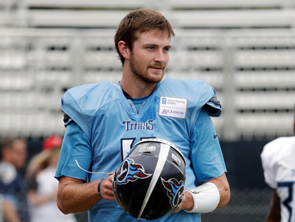 Luke Falk holds his helmet and walks on the field in Titans training camp in 2018.