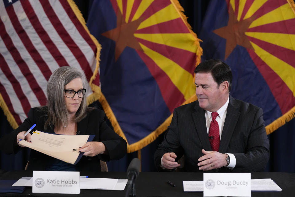 Katie Hobbs, the Democratic governor-elect and current secretary of state, left, passes canvass documents to Arizona Republican Gov. Doug Ducey, right, during the official certification for the Arizona general election canvass in a ceremony at the Arizona Capitol in Phoenix, Monday, Dec. 5, 2022. (AP Photo/Ross D. Franklin, Pool)