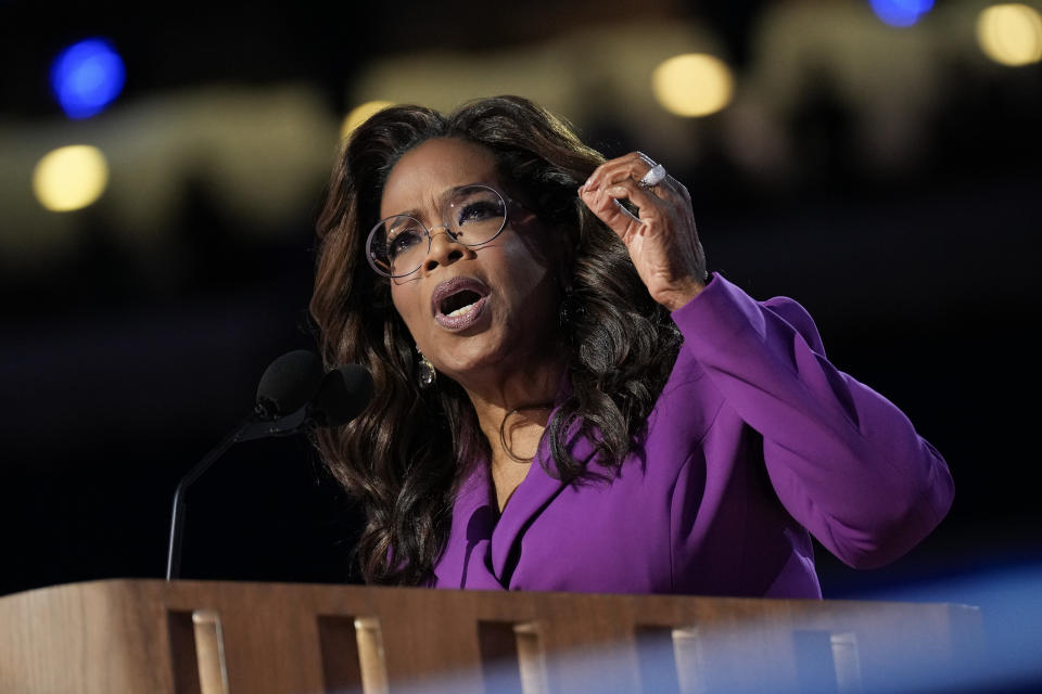 Oprah Winfrey steht an einem Podium und spricht leidenschaftlich, während sie mit der Hand gestikuliert. Sie trägt eine Brille und ein formelles Outfit