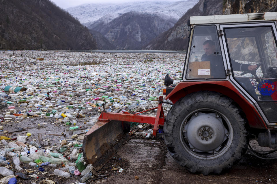 A worker uses a tractor to push the waste back in the Drina river near Visegrad, Bosnia, Wednesday, Jan. 10, 2024. Tons of waste dumped in poorly regulated riverside landfills or directly into the rivers across three Western Balkan countries end up accumulating during high water season in winter and spring, behind a trash barrier in the Drina River in eastern Bosnia. (AP Photo/Armin Durgut)