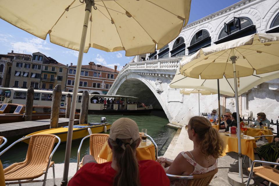 Customers sit at a cafe, in Venice, Italy, Thursday, June 17, 2021. After a 15-month pause in mass international travel, Venetians are contemplating how to welcome visitors back to the picture-postcard canals and Byzantine backdrops without suffering the indignities of crowds clogging its narrow alleyways, day-trippers perched on stoops to imbibe a panino and hordes of selfie-takers straining for a spot on the Rialto Bridge or in front of St. Mark’s Basilica. (AP Photo/Luca Bruno)