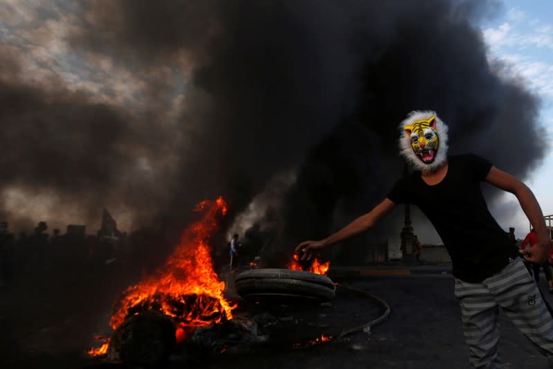 A masked protester throws a tire into fire during ongoing anti-government protests in Basra