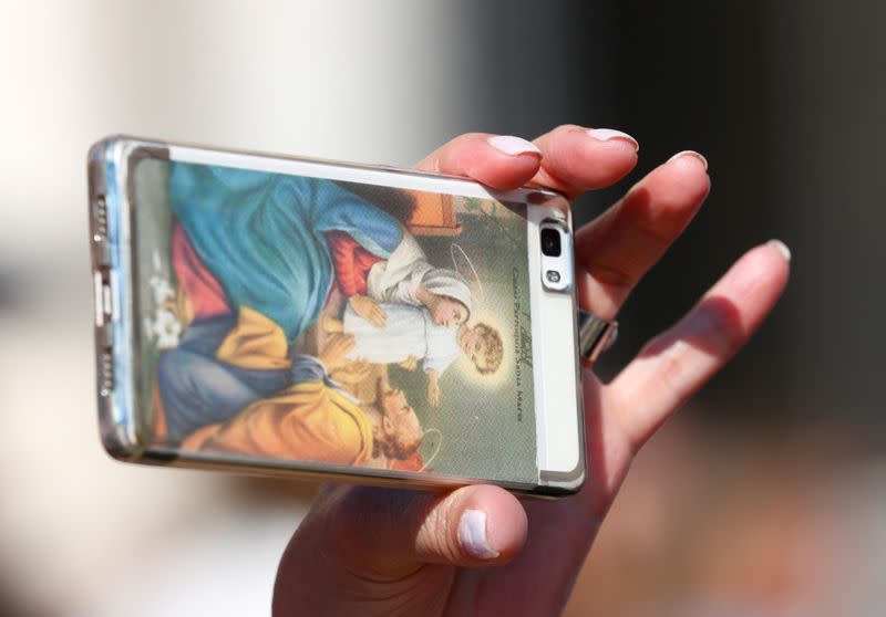 FILE PHOTO: A worshipper uses a phone with a cover depicting Holy Family as Pope Francis arrives to lead the Wednesday general audience in Saint Peter's square at the Vatican