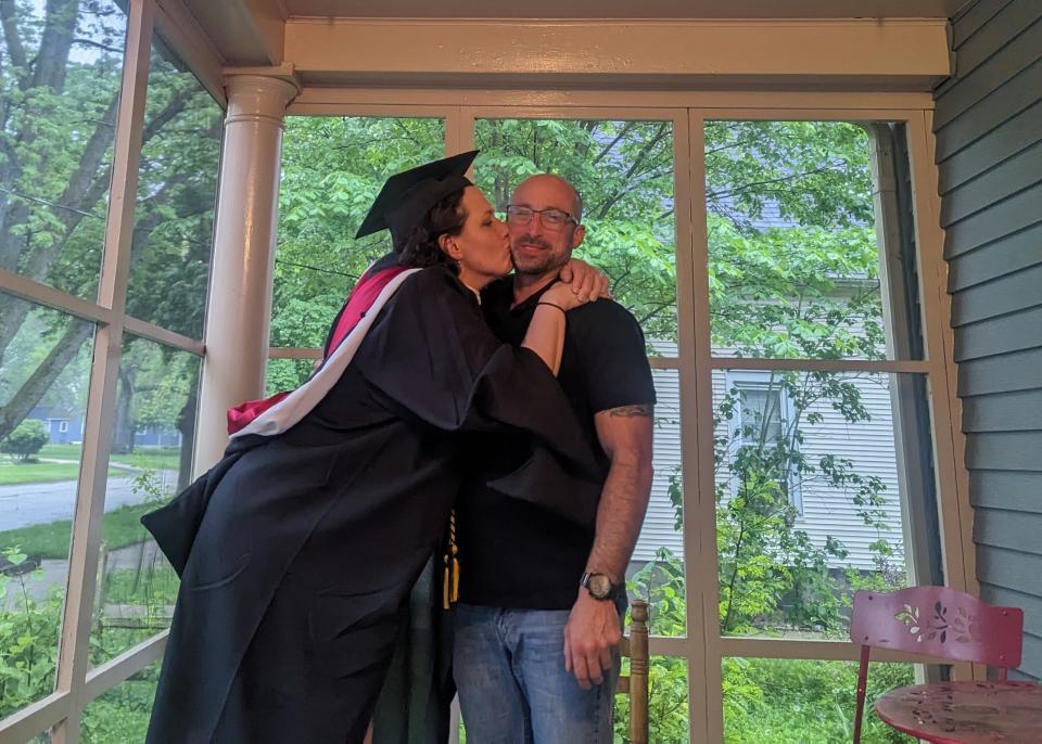 Nia Springer-Norris wearing a cap and gown kissing her partner Tom on the cheek on an enclosed porch.