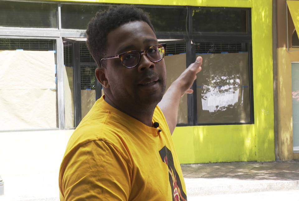 King Williams gestures at the former site of Alonzo Herndon’s barbershop that was destroyed by a mob in 1906 on June 10, 2022 in Atlanta. Williams, a journalist, gives tours describing what happened during the Atlanta Race Massacre. (AP Photo/Sharon Johnson)