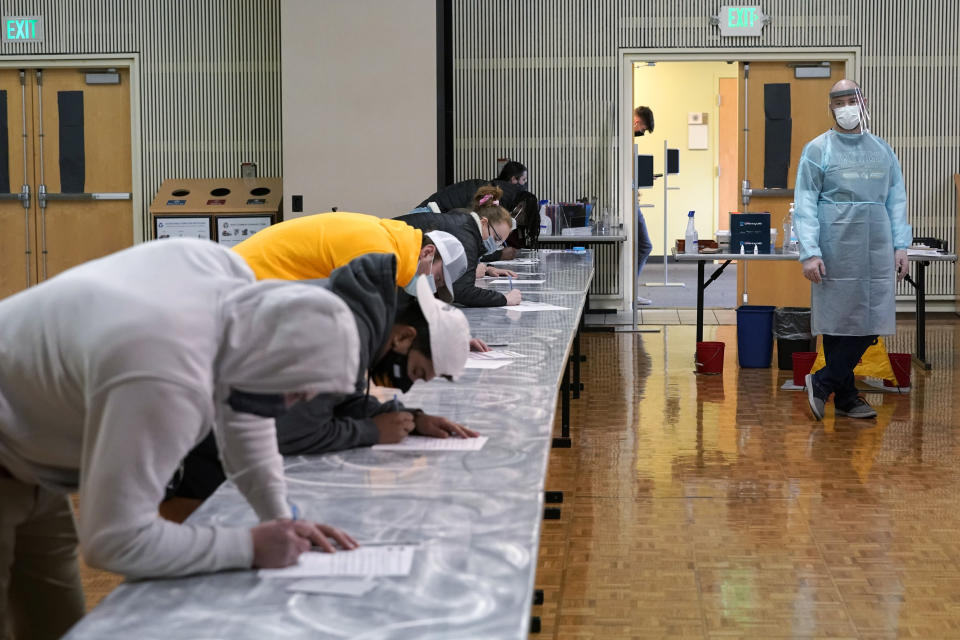 Brant McAdams, right, football coach at Pacific Lutheran, wears personal protective equipment as he watches student-athletes fill out forms for their three-times-a-week COVID-19 tests, Wednesday, Feb. 3, 2021, on campus in Tacoma, Wash. There was never a chapter in any of the books on becoming a small NCAA college football coach that addressed administering COVID-19 tests in the midst of a pandemic, but now it's something he's doing to give his players the chance at a season. (AP Photo/Ted S. Warren)