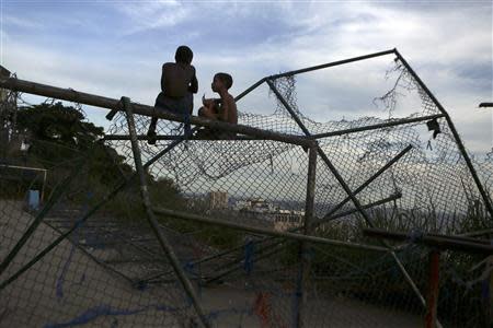 Two boys talk while sitting on the top of a soccer goalpost in bad condition at the Cantagalo slum in Rio de Janeiro March 13, 2014. REUTERS/Pilar Olivares