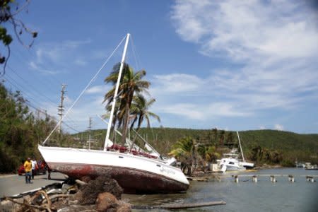 Men walk past a boat pushed onto a roadway by the winds of Hurricane Maria in Farjado, Puerto Rico October 12, 2017. REUTERS/Lucas Jackson