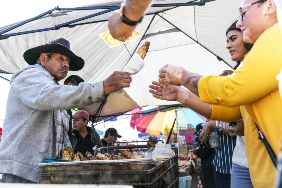 A man hands corn on the cob to two women.