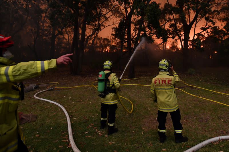 Fire fighting crews from the Rural Fire Service (RFS), NSW Fire and Rescue and National Parks and Wildlife Service (NPWS) officers fight a bushfire encroaching on properties near Lake Tabourie