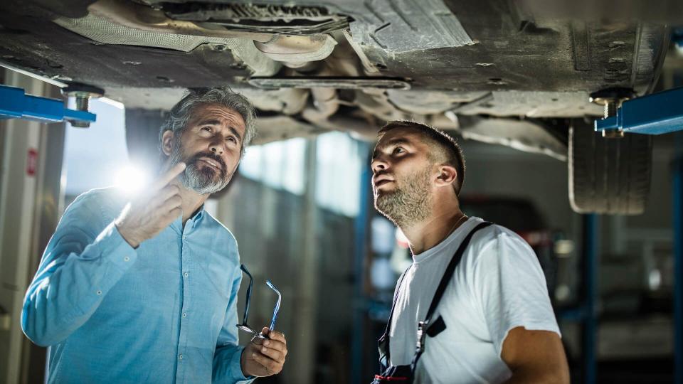 Mid adult customer and auto repairman analyzing chassis in a workshop.