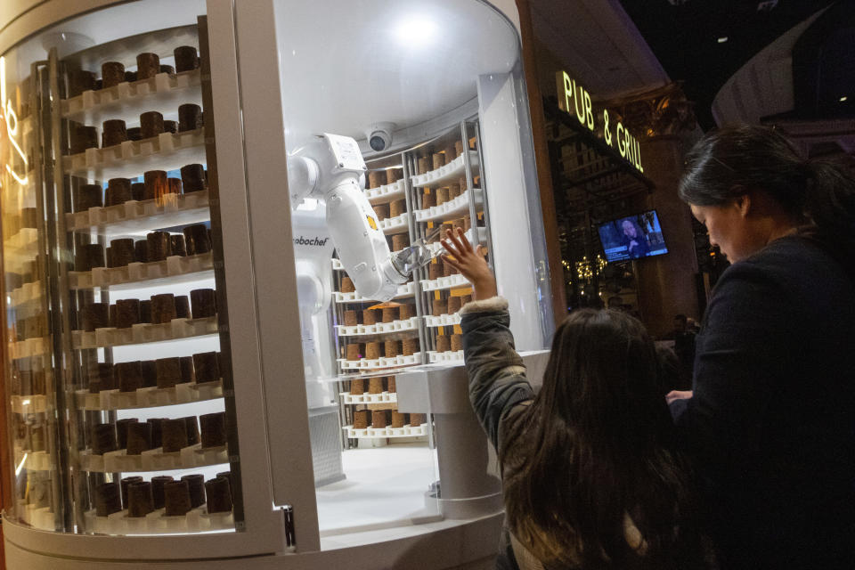A child waves to a robot dessert booth at Caesars Palace, Thursday, Jan. 11, 2024, in Las Vegas. Chef-like robots and barista bots caused a stir at the annual CES technology trade show in Las Vegas, putting a spotlight on casino union workers' fears that jobs could be at risk in the age of artificial intelligence. (AP Photo/ Ty ONeil)