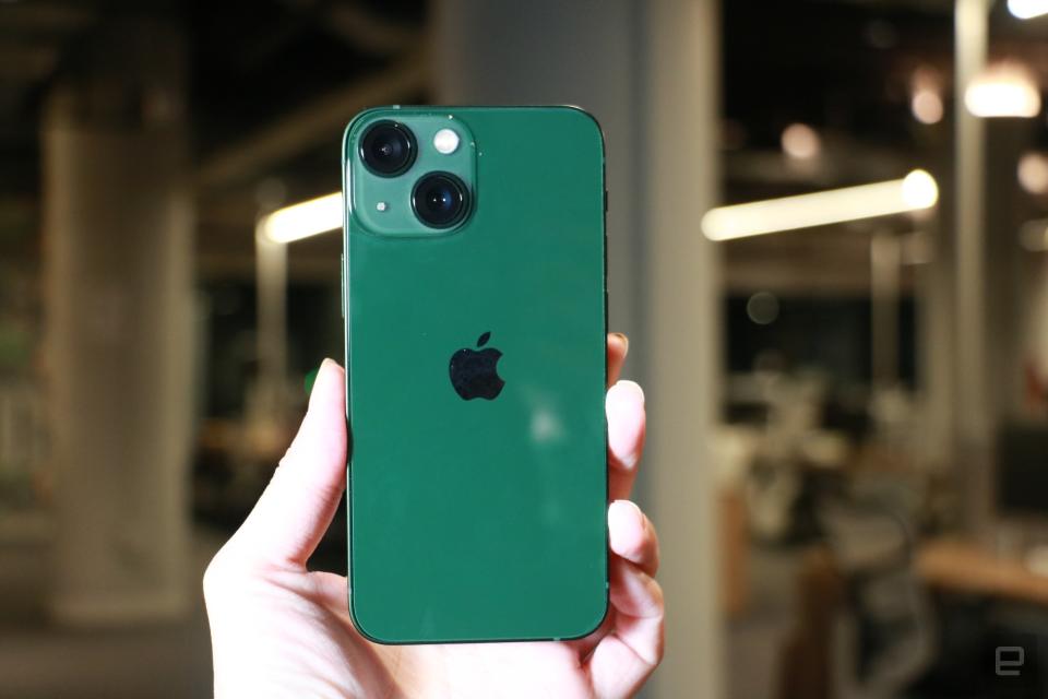 <p>A green iPhone 13 held up against a blurred background.</p>
