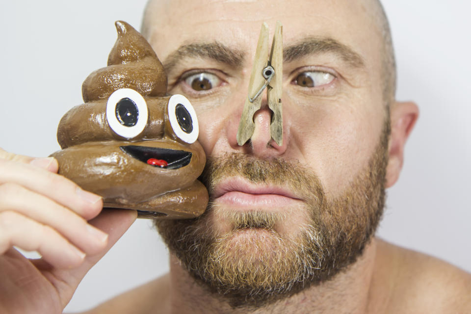Man holding poop emoji toy near his face, clothespin on nose, humorous expression