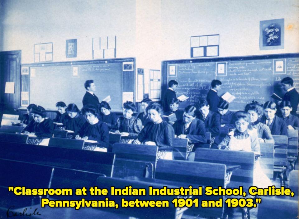 Historic classroom photo showing students and a teacher in a late 19th to early 20th-century setting, with students reading and writing