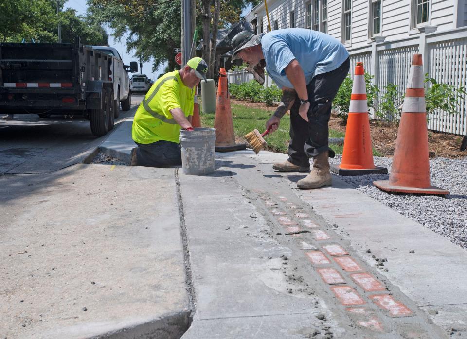 Brian Murphy and Brandon Burgans, employees with the city of Pensacola's Public Works and Facilities Department, work Tuesday to complete a section of the new markings for the "America's 1st Settlement Trail" on Florida Blanca Street in downtown Pensacola. The new trail will guide visitors to the city's historic sites and landmarks.