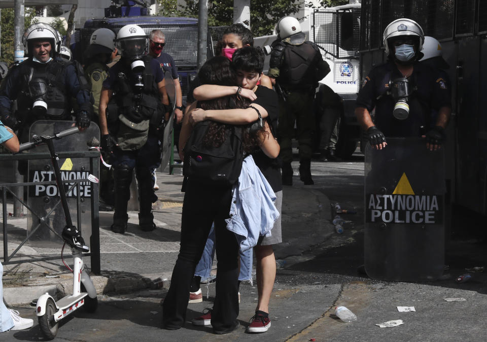 Backdropped by Greek riot police officers, protesters, of an anti-fascist rally, embrace each other following the announcement of the court verdict, outside the courthouse in Athens, Wednesday, Oct. 7, 2020. The court ruled that the far-right Golden Dawn party was operating as a criminal organization, delivering a landmark guilty verdict in a marathon five-year trial.The court ruled seven of the party's former lawmakers, including party leader Nikos Michaloliakos, were guilty of leading a criminal organization, while the others were guilty of participating in a criminal organization. .(AP Photo/Yorgos Karahalis)