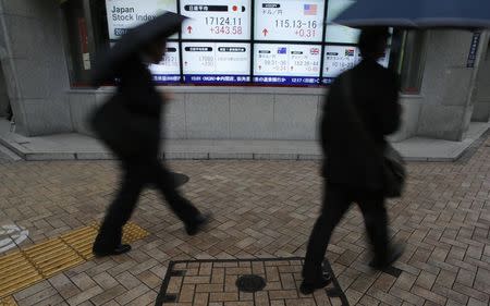 Pedestrians with umbrellas walk past an electronic board showing Japan's Nikkei average (top middle L) and the exchange rates between the Japanese yen and the U.S. dollar (top middle R), outside a brokerage in Tokyo November 11, 2014. REUTERS/Yuya Shino