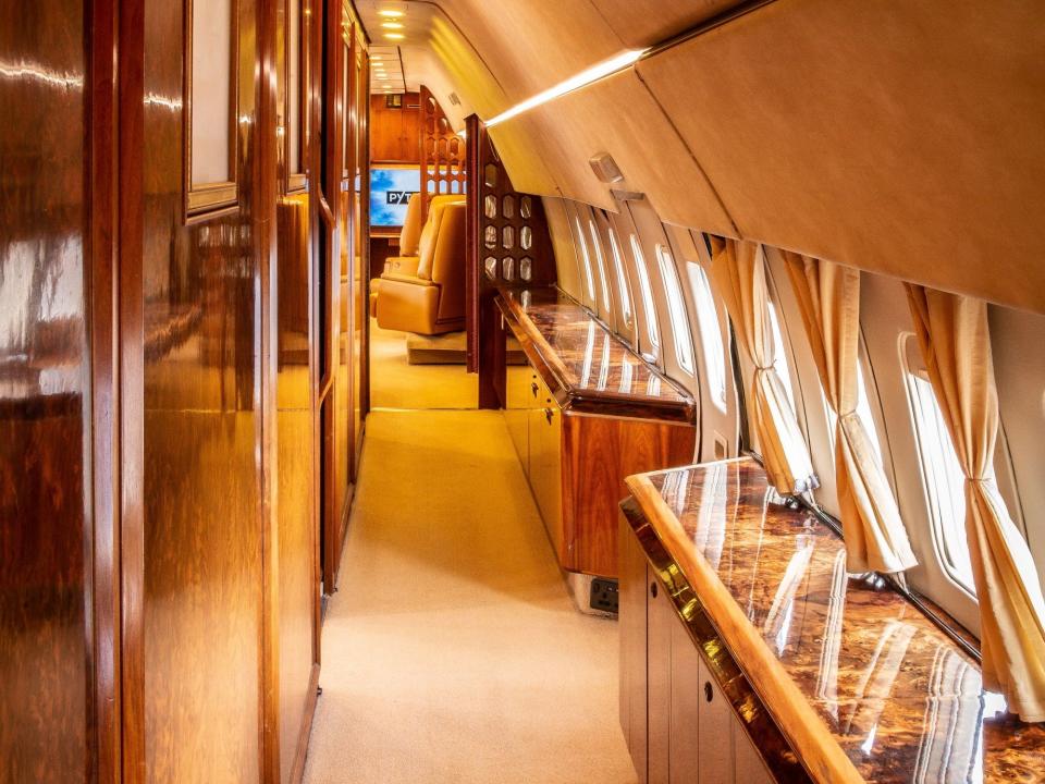 Inside the hallway leading from the back of the plane to the main lounge. The walls are brown with windows on the right side.