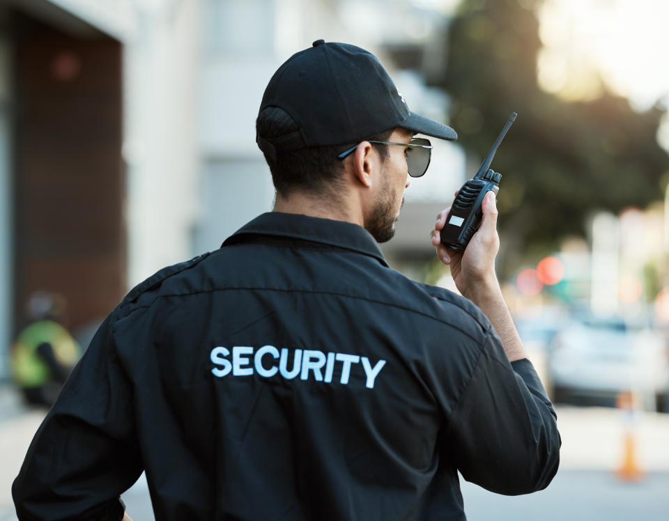 A uniformed security guard speaks into a walkie-talkie while on duty outdoors