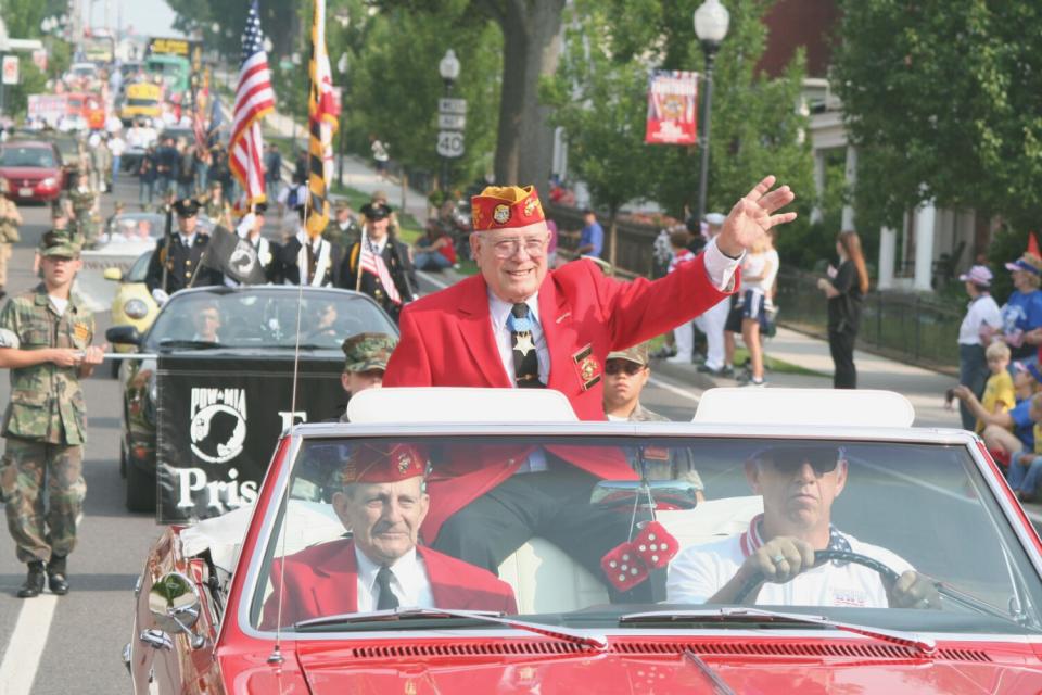 Hershel "Woody" Williams waves at spectators riding in the back of a convertible during a Fourth of July parade.