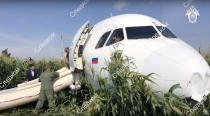 In this file image taken from a video distributed by Russian Investigative Committee, Investigative Committee employees works at a crash site of a Russian Ural Airlines' A321 plane is seen after an emergency landing in a cornfield near Ramenskoye, outside Moscow, Russia, Thursday, Aug. 15, 2019. The Russian pilot was being hailed as a hero Thursday for safely landing his passenger jet in a corn field after it collided with a flock of gulls seconds after takeoff, causing both engines to malfunction. While dozens of people on the plane sought medical assistance, only one was hospitalized. (The Investigative Committee of the Russian Federation via AP) EDS NOTE: Watermark placed on image at source translated as InvestCom