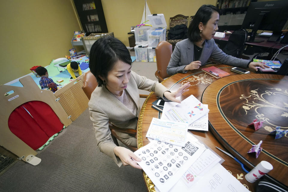 Keiko Kobayashi, left, and Sachiko Aoki, right, both employees of the staffing services company Pasona Inc., work as their children play in the background at the company's headquarters Monday, March 2, 2020, in Tokyo. Many Japanese schools were shut down Monday and spring holidays began unexpectedly early for children as part of a government-led measure to prevent further escalation of the coronavirus. The measure is a big burden and a headache for working mothers, especially those with small children or disabilities. (AP Photo/Eugene Hoshiko)