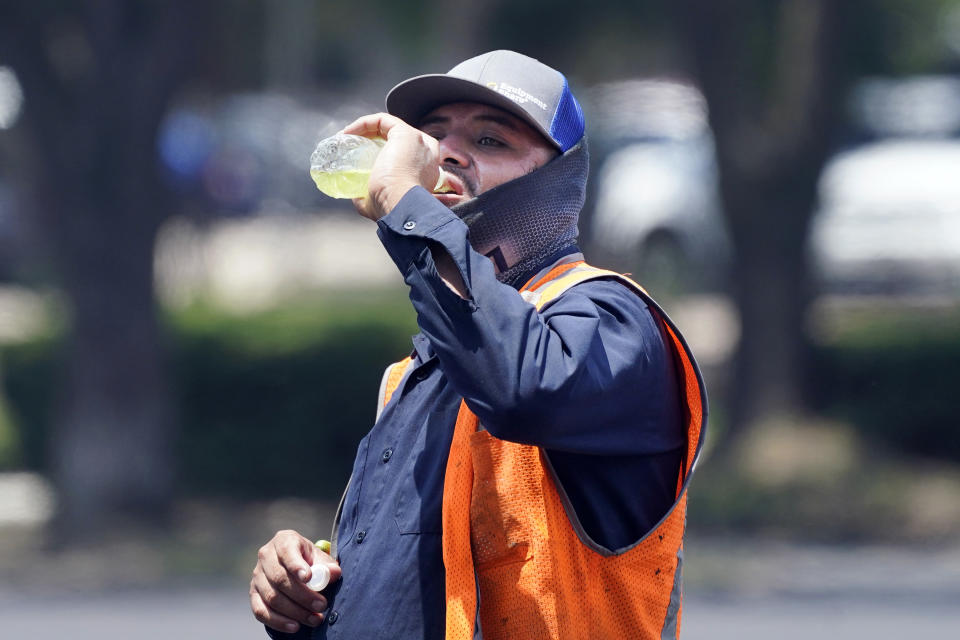 Standing in the mid afternoon heat, a worker takes a drink during a parking lot asphalt resurfacing job in Richardson, Texas, Tuesday, June 20, 2023. (AP Photo/LM Otero)