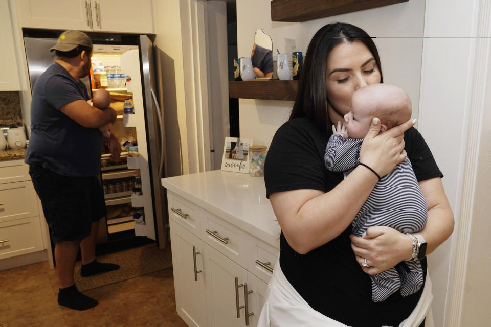 Lissette Fernandez kisses their newborn son Luca as her husband George holds their daughter Lexi, while while putting away their bottles, Tuesday, May 24, 2022, in Coral Gables, Fla. The Fernandez have family and friends from all over the county looking for formula for their newborn twins. (AP Photo/Marta Lavandier)