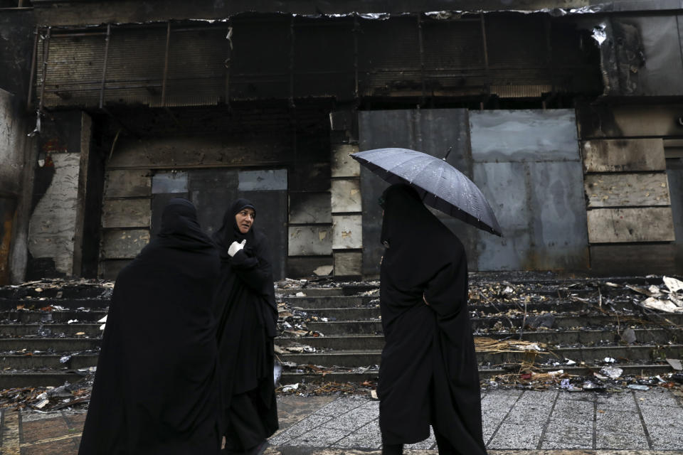 Women walk past a building damaged during recent protests, in Shahriar, Iran, some 40 kilometers (25 miles) southwest of the capital, Tehran, Wednesday, Nov. 20, 2019. Protests over government-set gasoline prices rising struck at least 100 cities and towns, spiraling into violence that saw banks, stores and police stations attacked and burned. (AP Photo/Vahid Salemi)