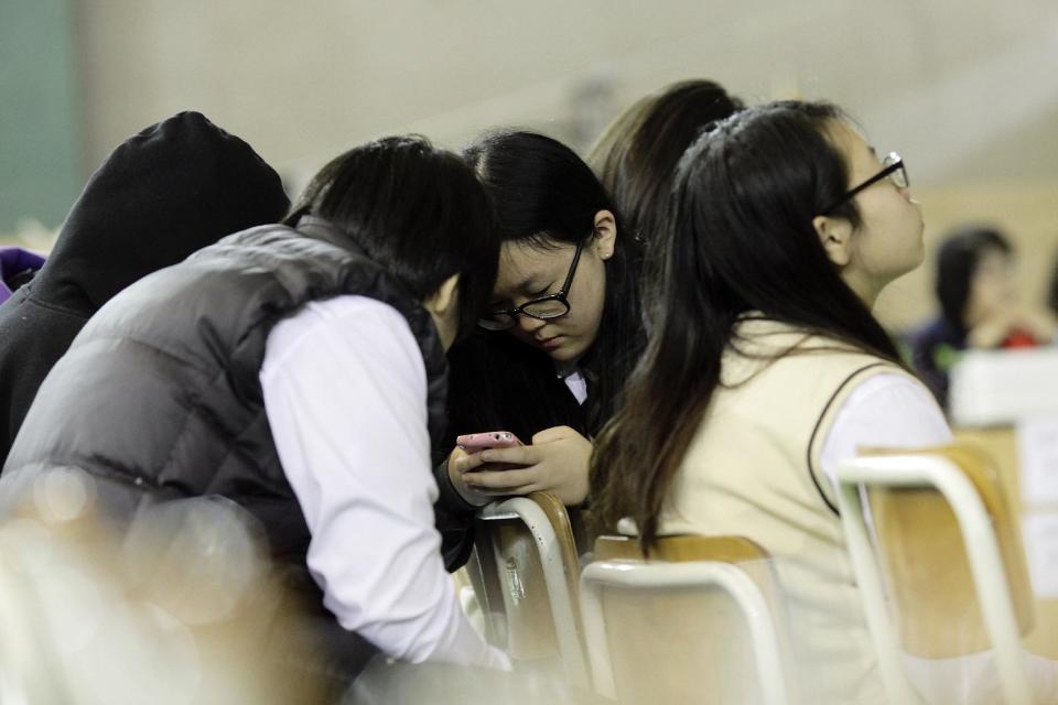 Students check a mobile phone for the latest news on the ferry that sank Wednesday, which was carrying 475 people aboard, including 325 students, at an auditorium in Danwon High School in Ansan, South Korea, Thursday, April 17, 2014. Strong currents, rain and bad visibility hampered an increasingly anxious search Thursday for 287 passengers, many thought to be high school students, still missing more than a day after their ferry flipped onto its side and sank in cold waters off the southern coast of South Korea. (AP Photo/Woohae Cho)