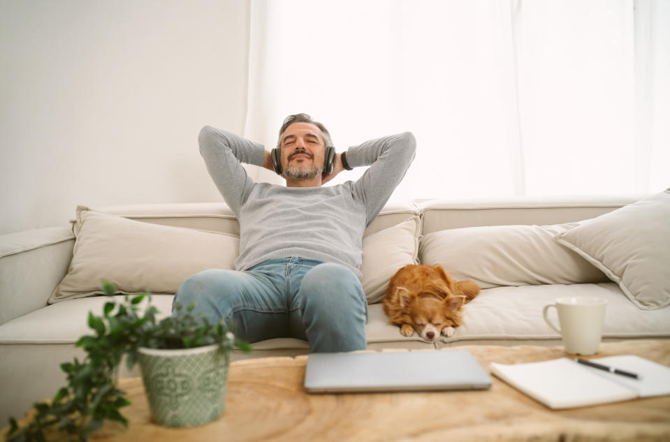 man and his dog on the couch as he smiles and listens to his headphones