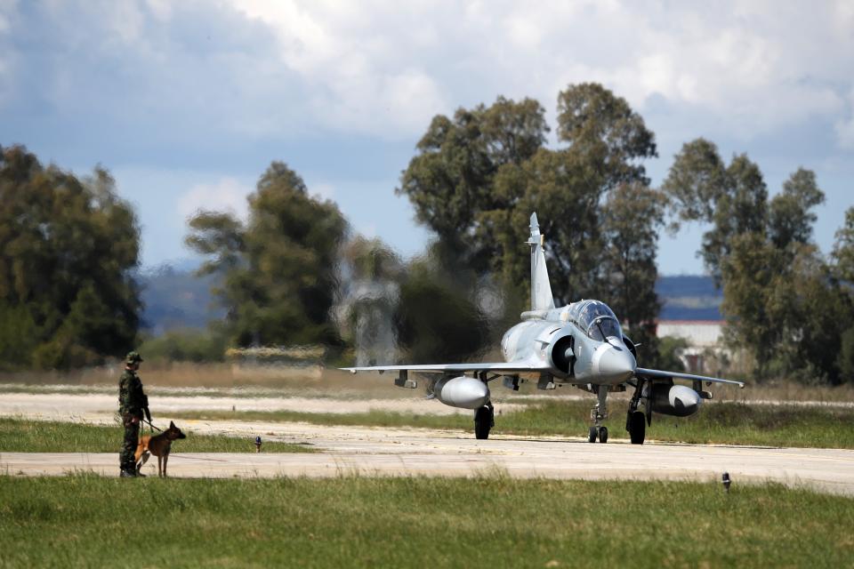 A Greek crew of a Mirage 2000-5 taxis as a soldier with a dog guards at Andravida air base, about 279 kilometres (174 miles) southwest of Athens, Tuesday, April 20, 2021. Greece vowed Tuesday to expand military cooperation with traditional NATO allies as well as Middle Eastern powers in a race to modernize its armed forces and face its militarily assertive neighbor Turkey. (AP Photo/Thanassis Stavrakis)