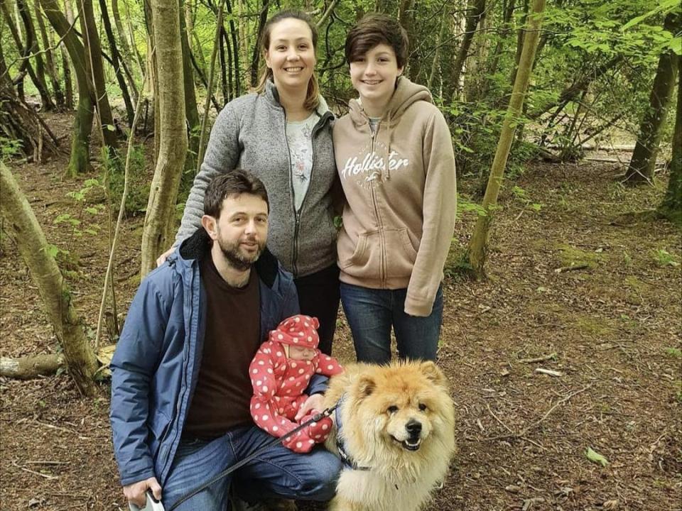 A family of four standing in a wood with a dog.