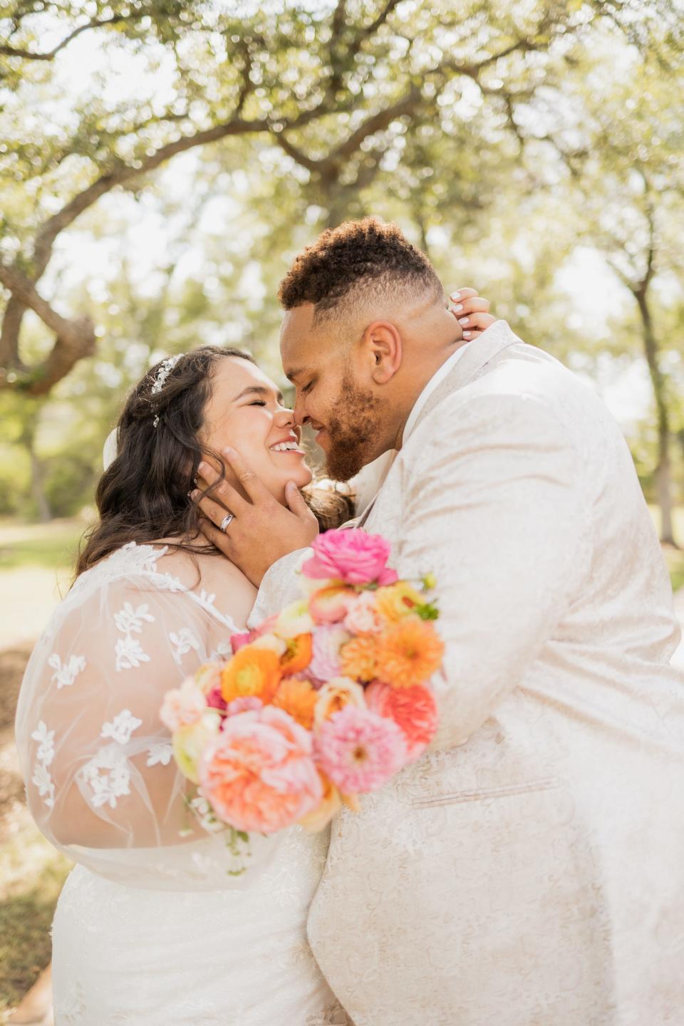 A bride and groom lean in to each other to kiss in front of trees on their wedding day.