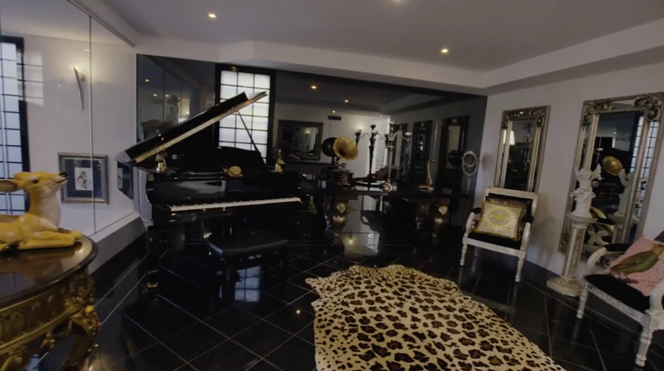 A grand piano is featured in the living room, along with glossy mirrors and a leopard print rug