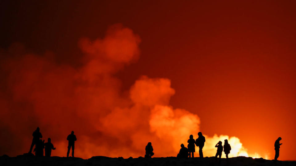 A group of people view the volcano with orange background behind them