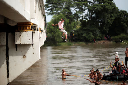 A Honduran migrant, part of a caravan trying to reach the U.S., jumps from the bridge that connects Mexico and Guatemala to avoid the border checkpoint in Ciudad Hidalgo, Mexico, October 19, 2018. REUTERS/Ueslei Marcelino
