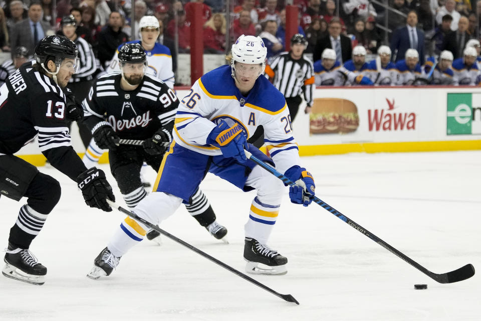 Buffalo Sabres defenseman Rasmus Dahlin (26) looks to pass against New Jersey Devils center Nico Hischier (13) during first period of an NHL hockey game, Tuesday, April 11, 2023, in Newark, N.J. (AP Photo/John Minchillo)