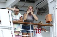 Passengers react from the MS Westerdam docked at the port of Sihanoukville, Cambodia, Saturday, Feb. 15, 2020. After being stranded at sea for two weeks because five ports refused to allow their cruise ship to dock, the passengers of the MS Westerdam were anything but sure their ordeal was finally over. (AP Photo/Heng Sinith)