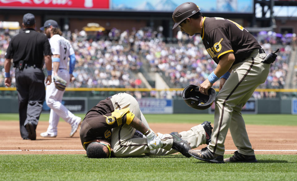 San Diego Padres first base coach David Macias, right, looks to help Manny Machado after Machado was injured while trying to run out a ground ball hit to Colorado Rockies starting pitcher Antonio Senzatela in the first inning of a baseball game Sunday, June 19, 2022, in Denver. Machado, who was out on the play, had to be helped from the field. (AP Photo/David Zalubowski)