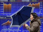 A pedestrian holding an umbrella walks past an electronic board displaying graphs of the recenent movement of Japan's Nikkei average outside a brokerage in Tokyo December 19, 2013. REUTERS/Yuya Shino